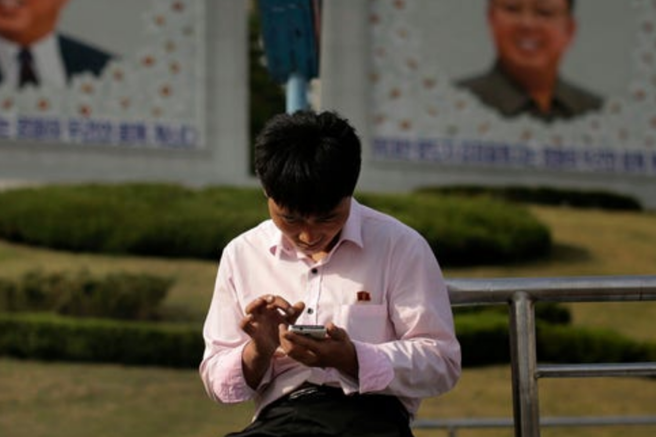 مواطن كوري شمالي يجلس أمام صورة زعيم كيم و أبية أيل وهو يتصح هاتفة 5 مايو 2015